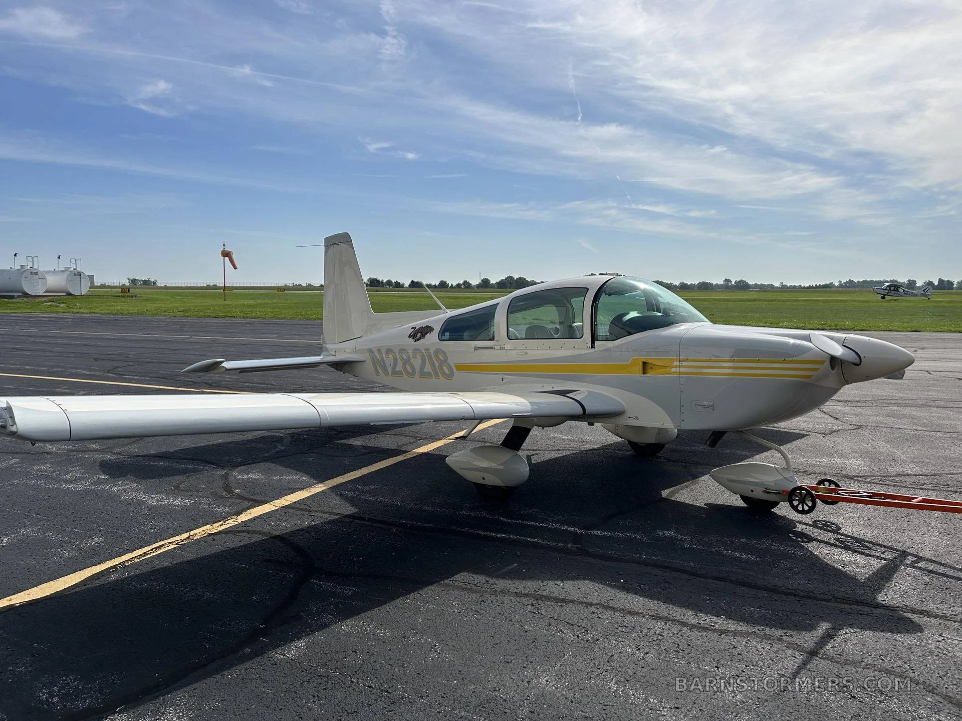 A white and yellow Grumman AA-5B Tiger aircraft with tail number N28218 parked on an asphalt ramp under a partly cloudy sky.