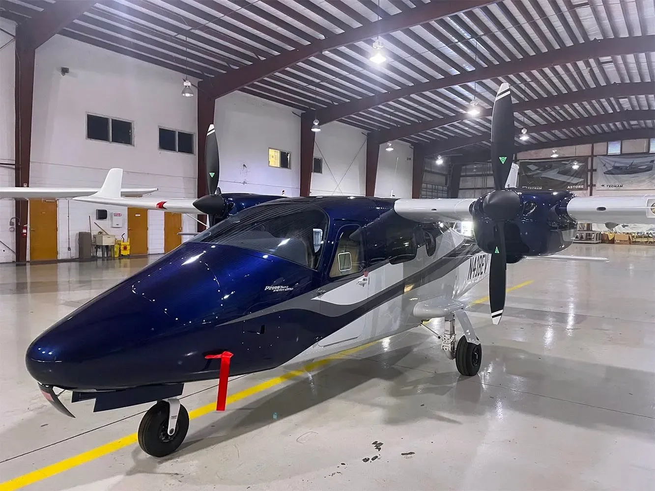 A sleek blue and silver twin-engine aircraft with registration N108EY parked in a well-lit hangar.