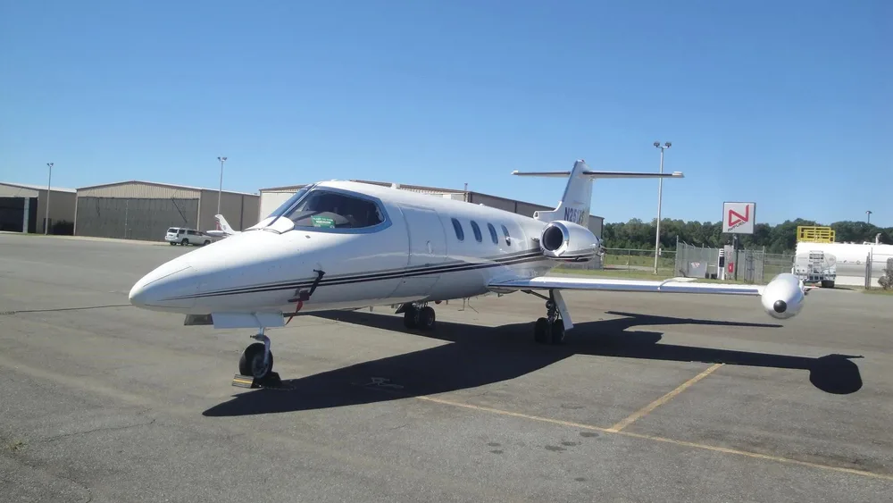 A white Learjet N251TS is parked on an airport tarmac on a sunny day.