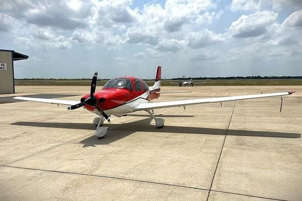 A red and white Cirrus SR22 aircraft, registration N47TP, parked on an airport apron under a partly cloudy sky.