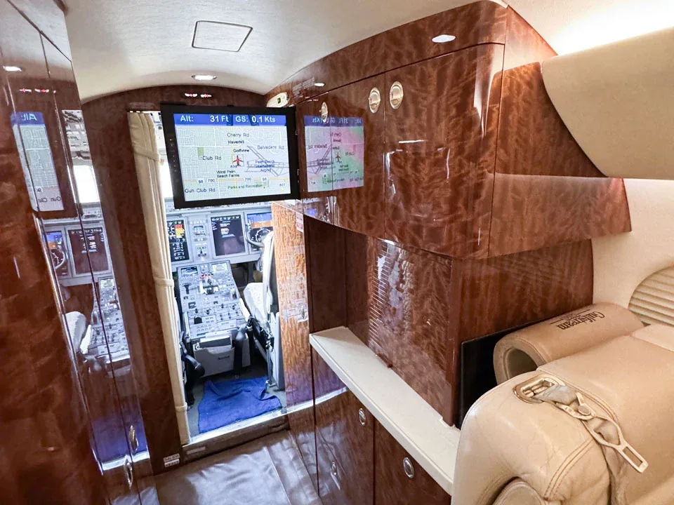 A private jet's cabin with a large monitor displaying a flight map, and a glimpse of the cockpit.