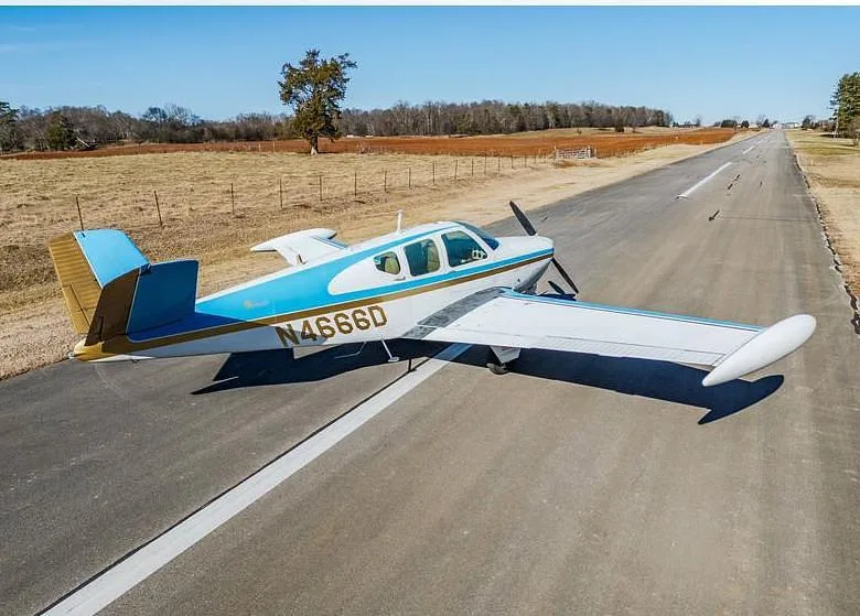 A side-rear view of the white and blue single-engine aircraft N4666D on a long asphalt runway.