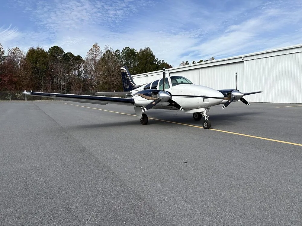 A white and dark blue twin-engine aircraft with registration N55SE is parked on the tarmac, viewed from the front right.