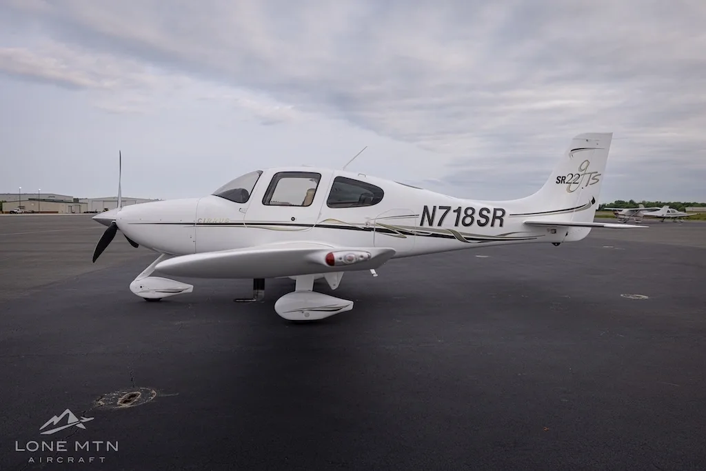 Side view of a white Cirrus SR22T aircraft with black and gold accents parked on an asphalt tarmac.
