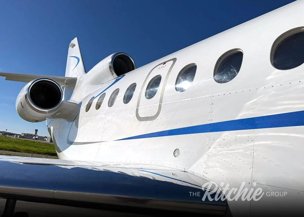 A close-up view of the white Dassault Falcon fuselage, showing windows, an entry door, and an engine.