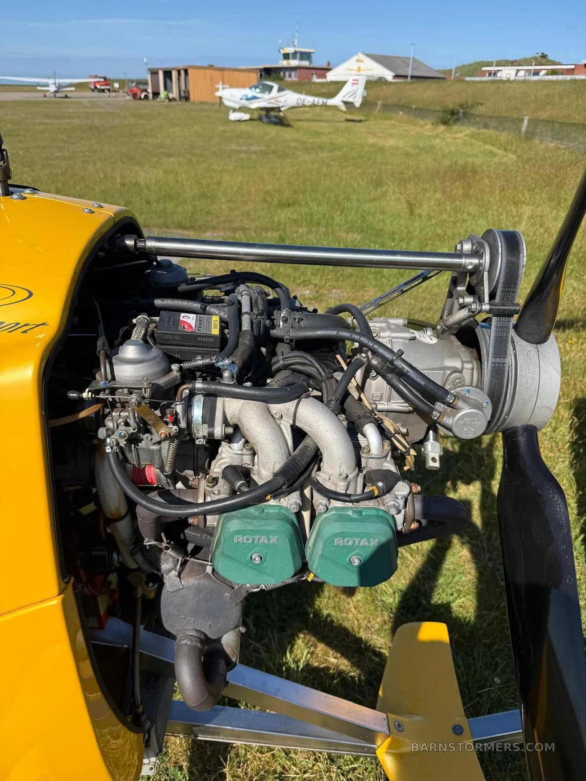 A close-up of the Rotax engine of a yellow MTO Sport autogyro, showing its components and green valve covers.