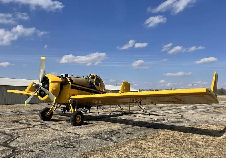 A yellow agricultural aircraft with black stripes is parked on an asphalt runway under a blue sky.