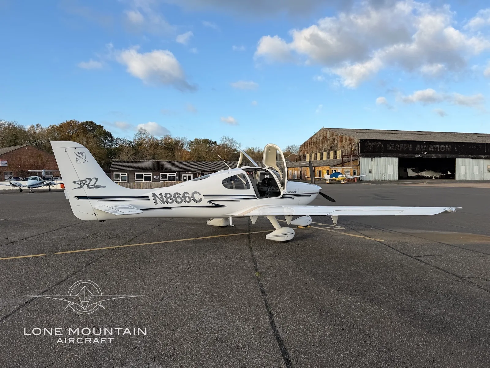 A white Cirrus SR22 aircraft with black and grey stripes, registration N866C, parked on an asphalt apron with its doors open.
