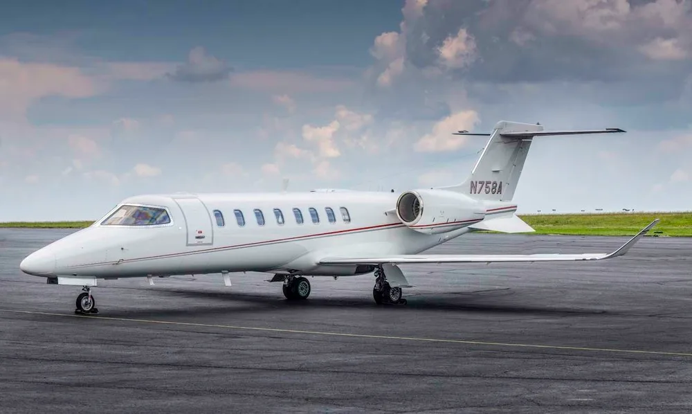 A white Learjet 75 with red pinstripes, tail number N758A, is parked on an asphalt tarmac under a cloudy sky.