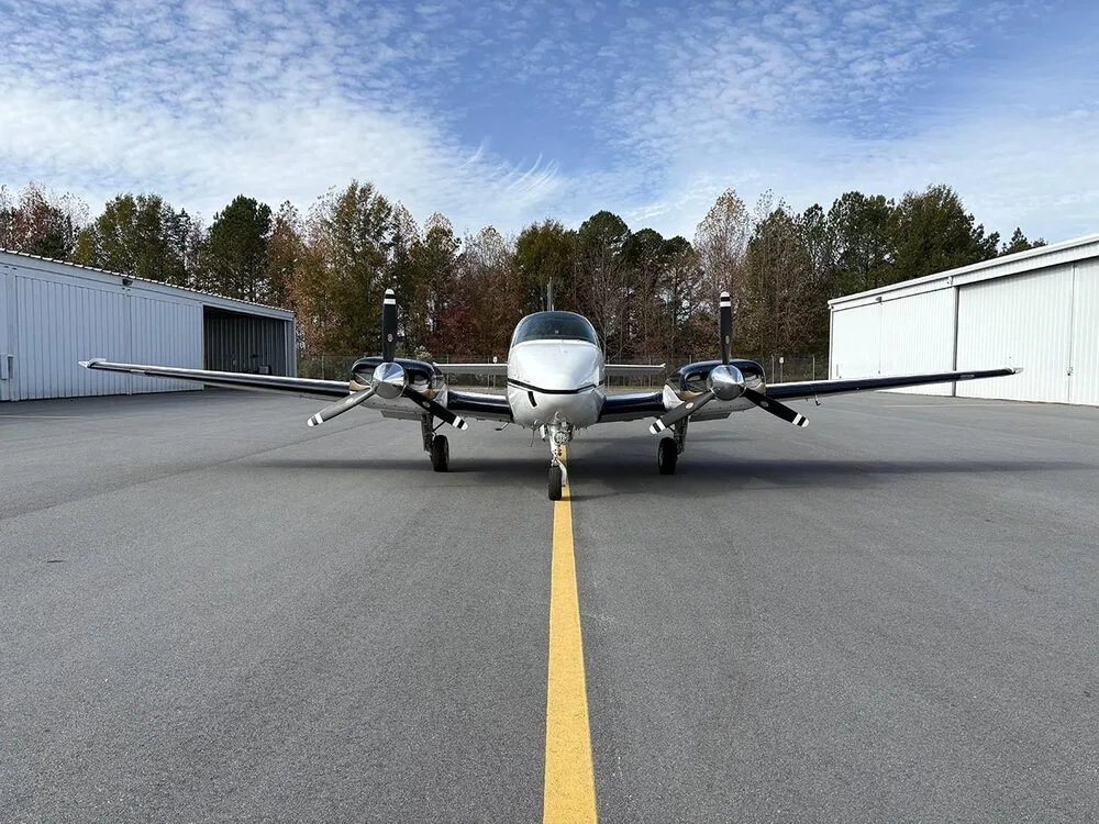 A white and dark blue twin-engine aircraft with registration N55SE is parked head-on on the tarmac, centered on a yellow line.