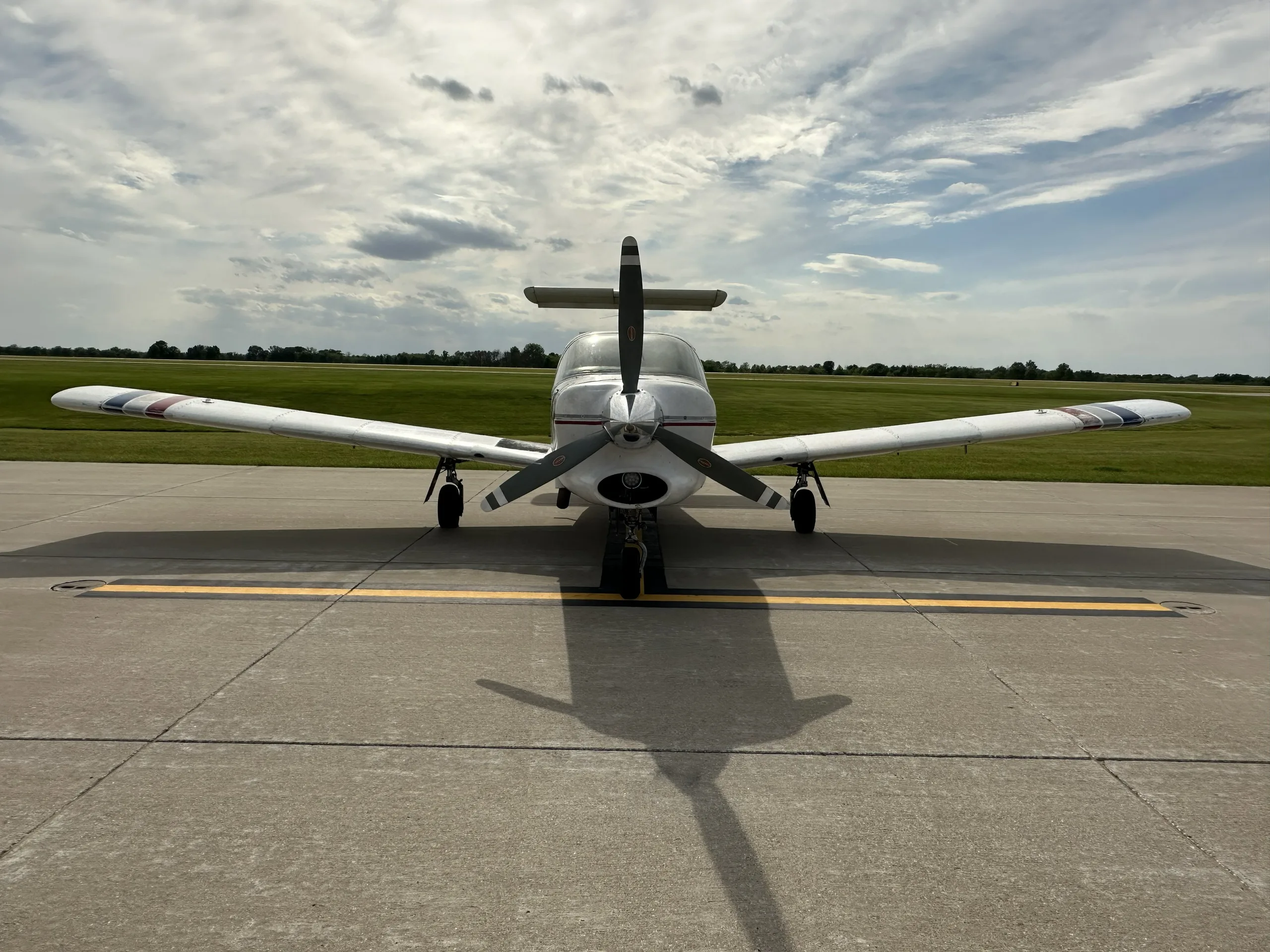A front view of a white Piper Turbo Lance II aircraft with a propeller, parked on an airfield.