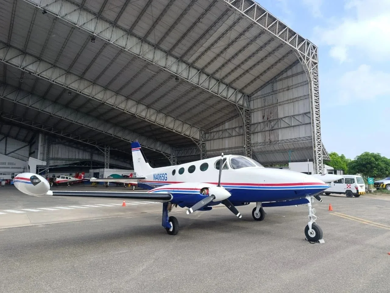 A white and blue Cessna 340 twin-engine aircraft with red stripes parked in front of a large hangar.