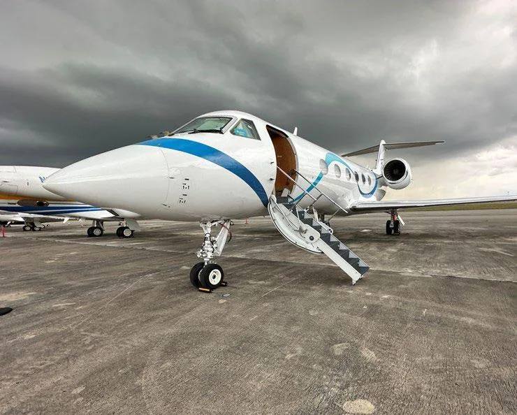 A Gulfstream G450 business jet with a white and blue wavy paint scheme parked on an airfield with its passenger door open.
