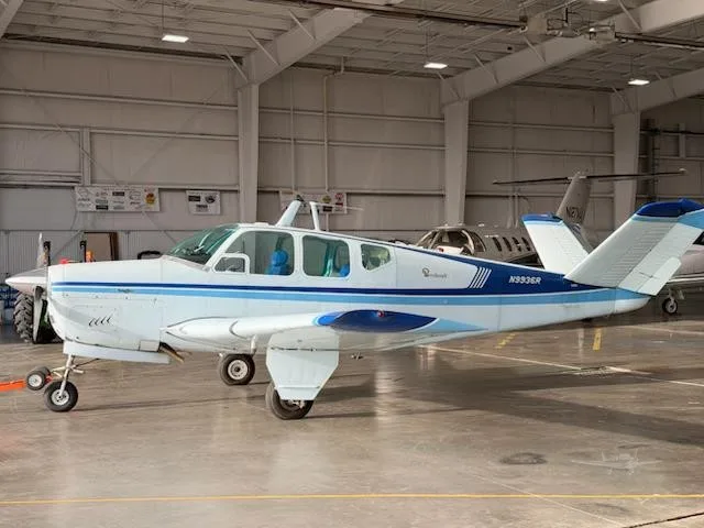 A white and blue Beechcraft Bonanza N9936R is parked inside a hangar.
