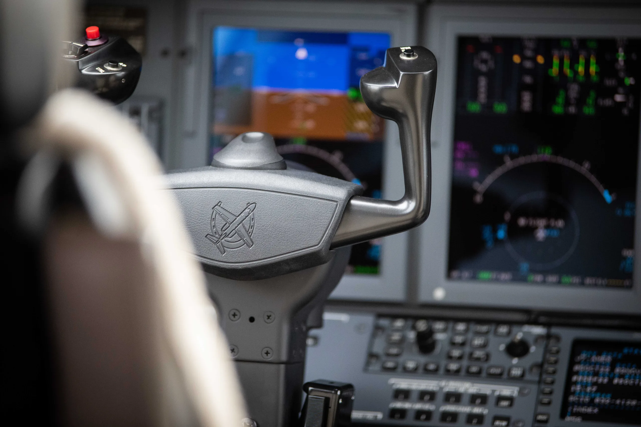 A close-up view of an aircraft's control yoke with a logo and digital instrument displays in the background.