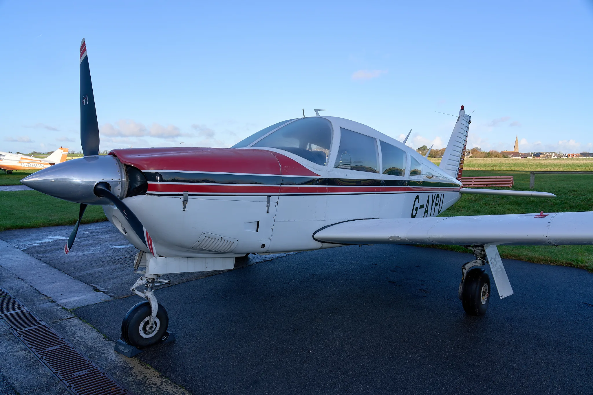 A close-up front-left view of the white and red Piper Cherokee G-AYPU on the tarmac.