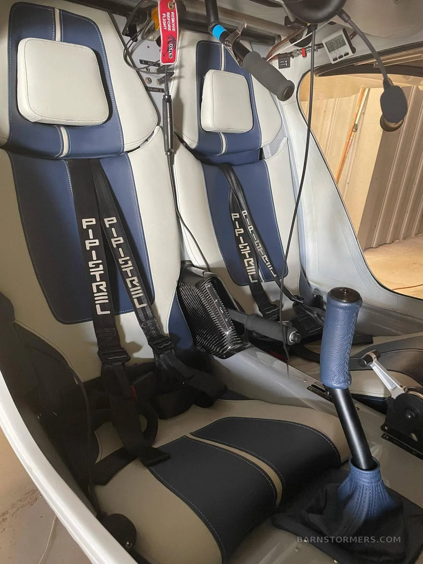 The interior of an aircraft cabin with two blue and white upholstered seats and harnesses.