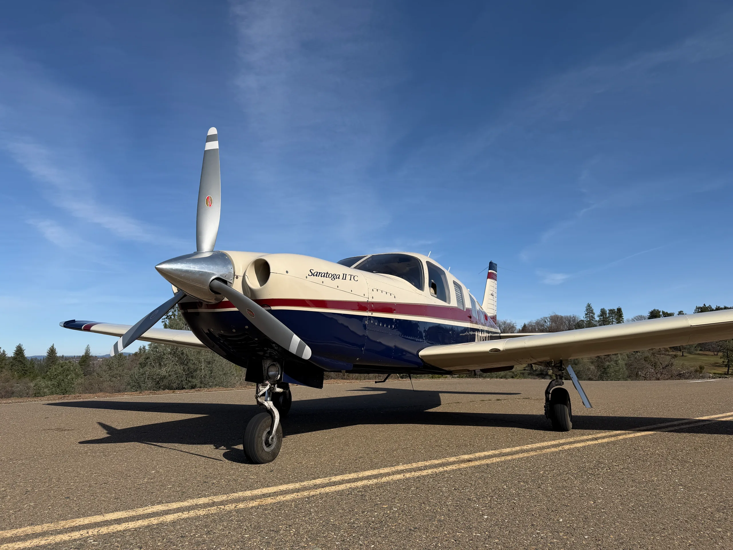 A low-angle front view of a Piper Saratoga II TC aircraft with a cream, blue, and red paint scheme on an asphalt surface.