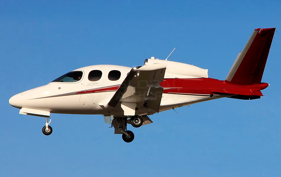 A white and red single-engine jet aircraft with landing gear extended flies against a clear blue sky.