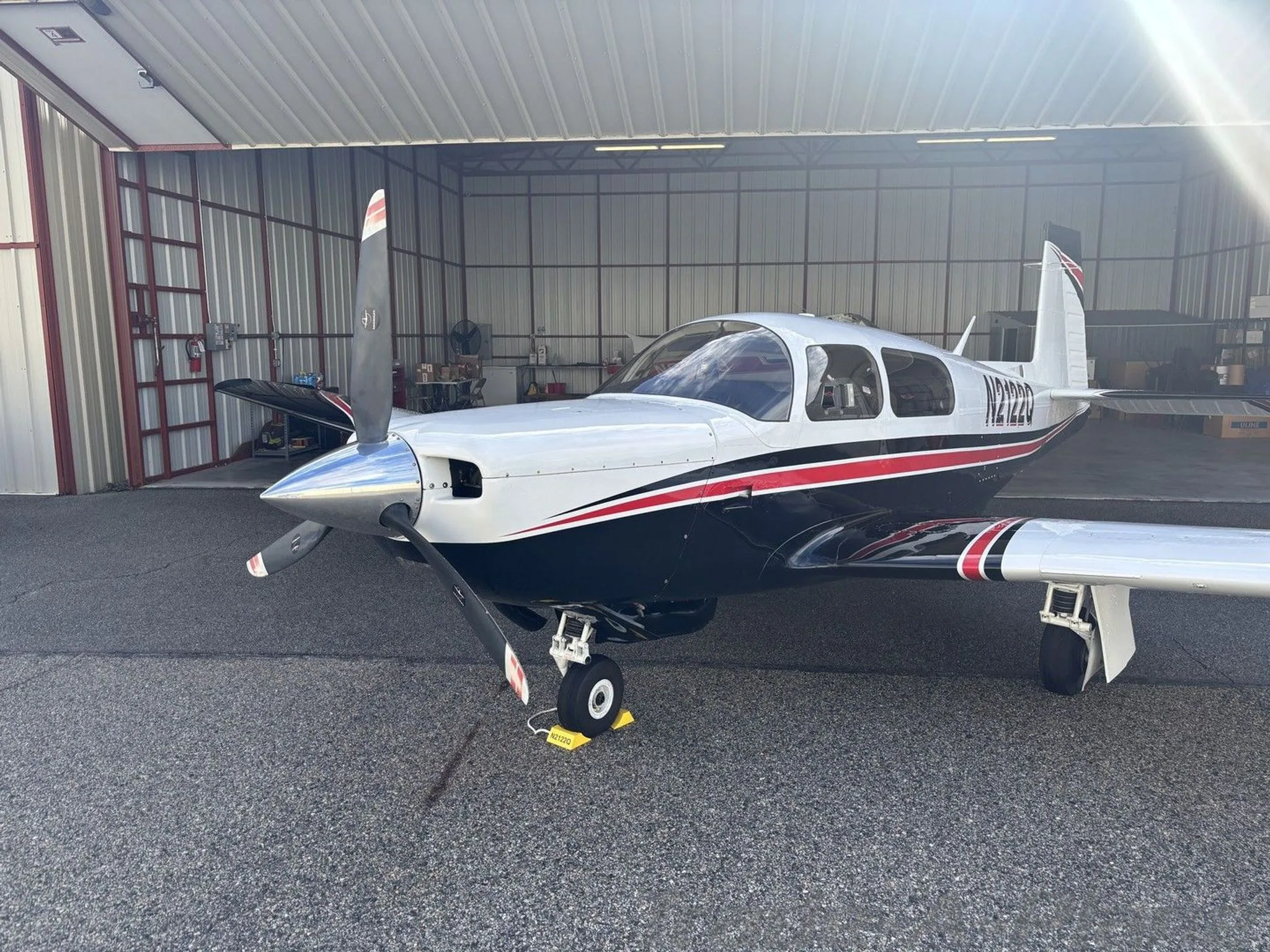A front-quarter view of a white and black Mooney M20K aircraft with red stripes, registration N2122Q, parked in a hangar.
