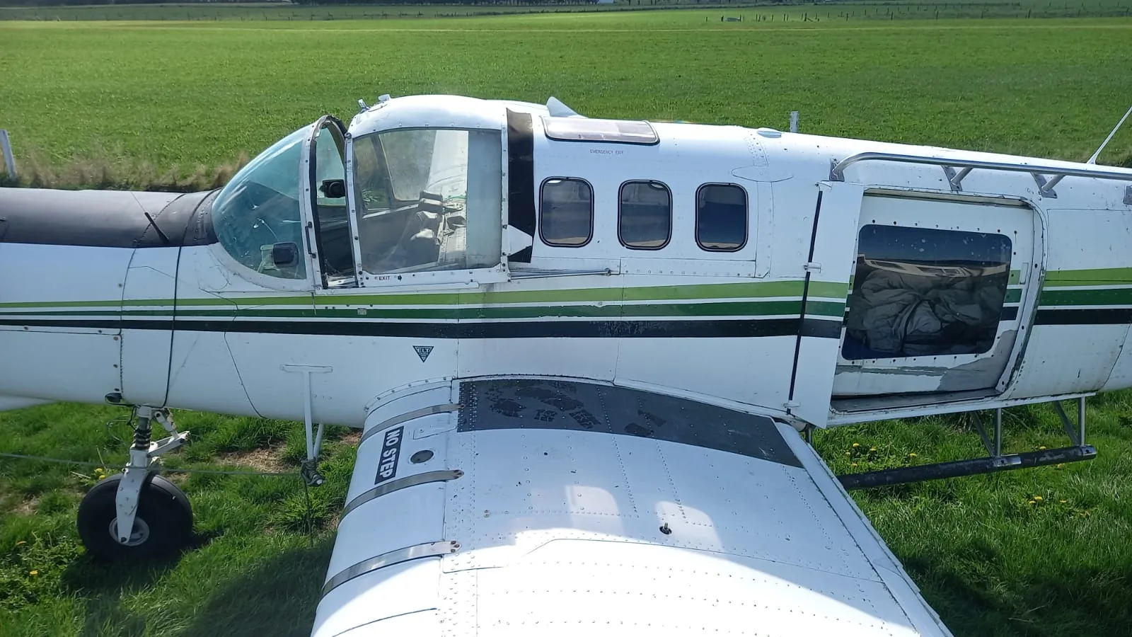 A side view of a white turboprop aircraft with green stripes, showing open cockpit and cabin doors, parked on a grassy field.