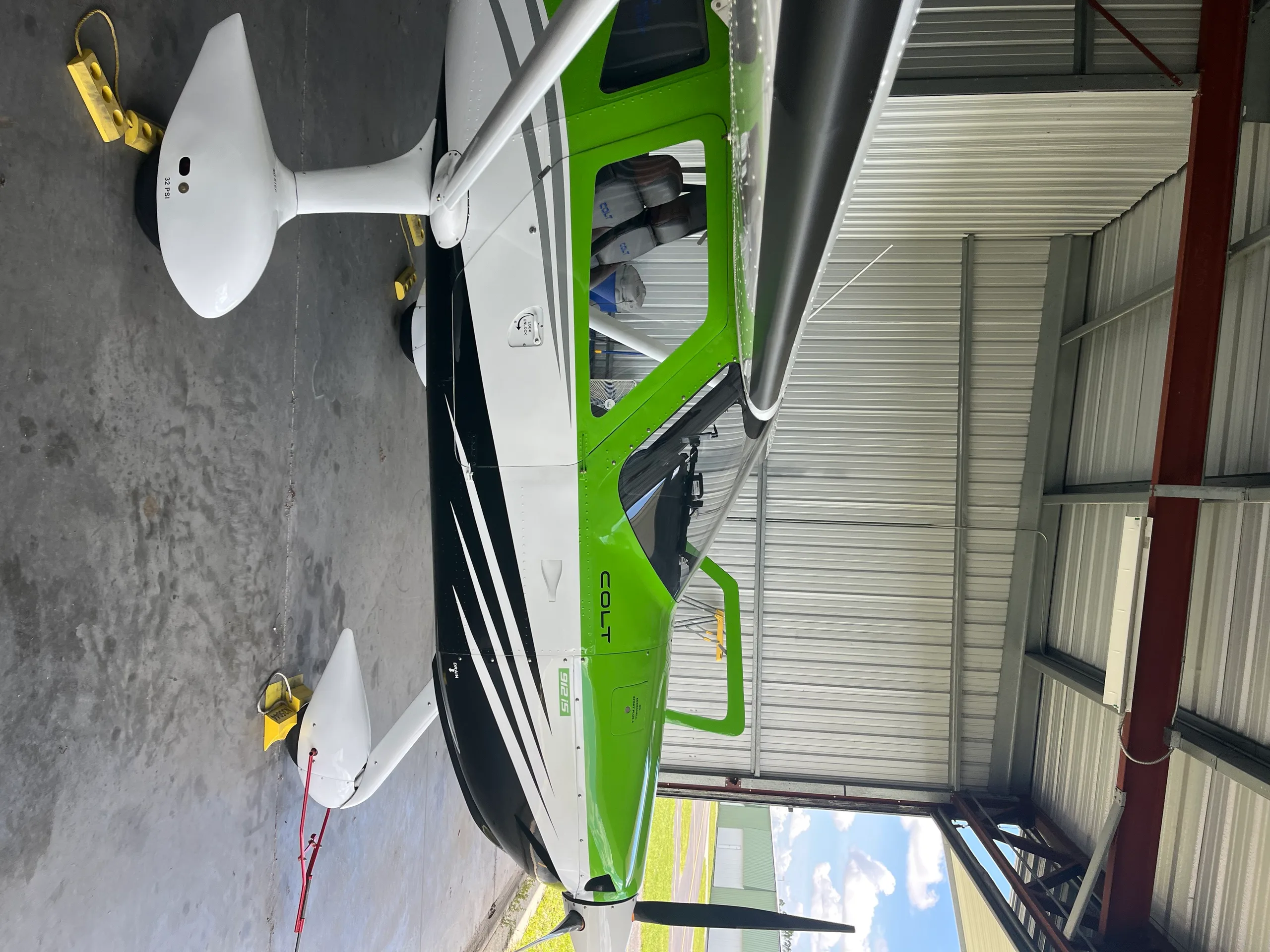 A side view of a green, white, and black Colt light sport aircraft parked in a hangar.