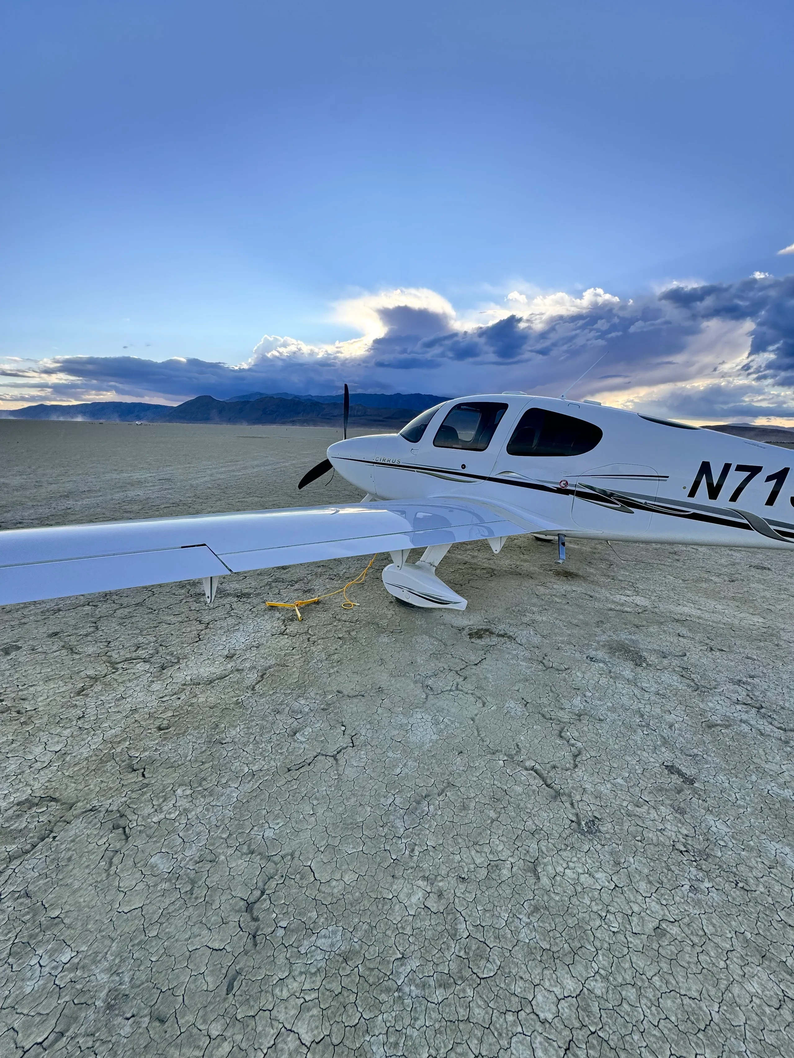 A close-up side view of a white Cirrus SR22T aircraft (N715WT) parked on a cracked dry lake bed.