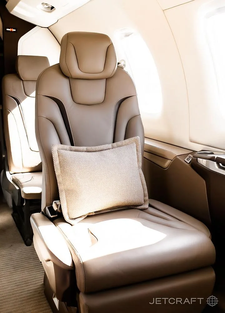A single tan leather aircraft cabin seat with a small textured pillow, illuminated by sunlight from a window.