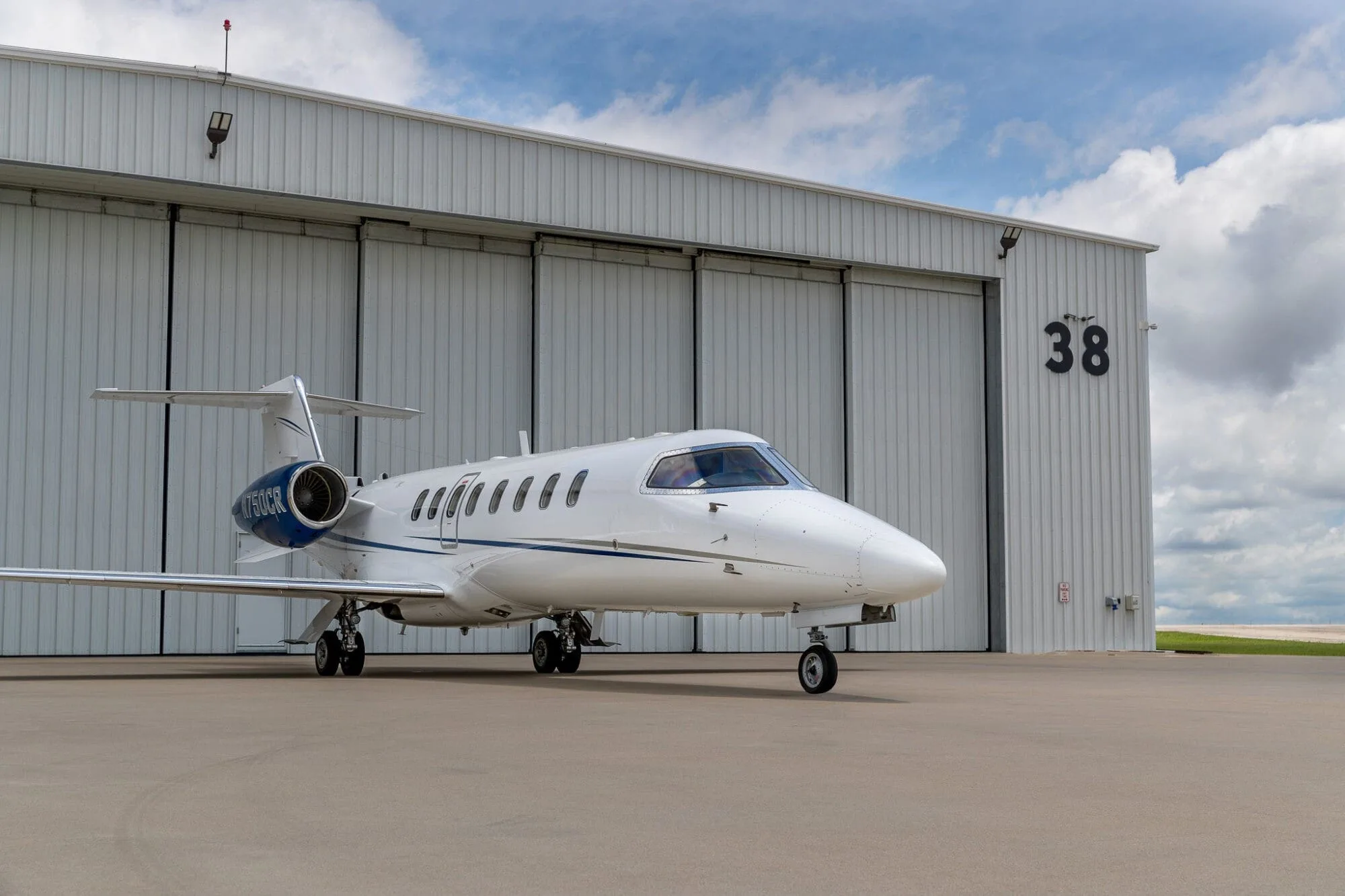 A white and dark blue business jet, registration N227WE, parked on an tarmac against a vibrant orange sunset.