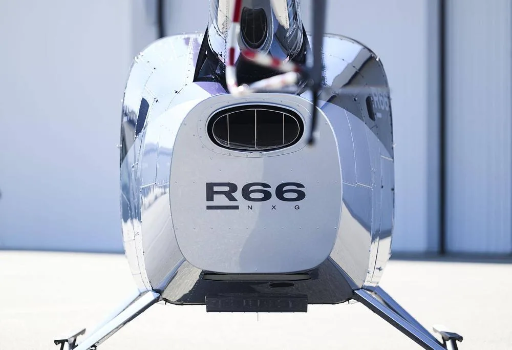 A close-up rear view of a silver and blue Robinson R66 NXG helicopter's tail section.