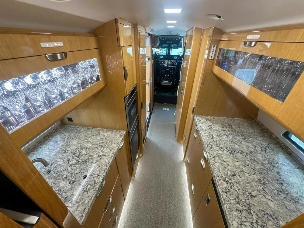 The aircraft galley features marble-patterned countertops, wooden cabinetry, illuminated glass displays, and a view towards the cockpit.