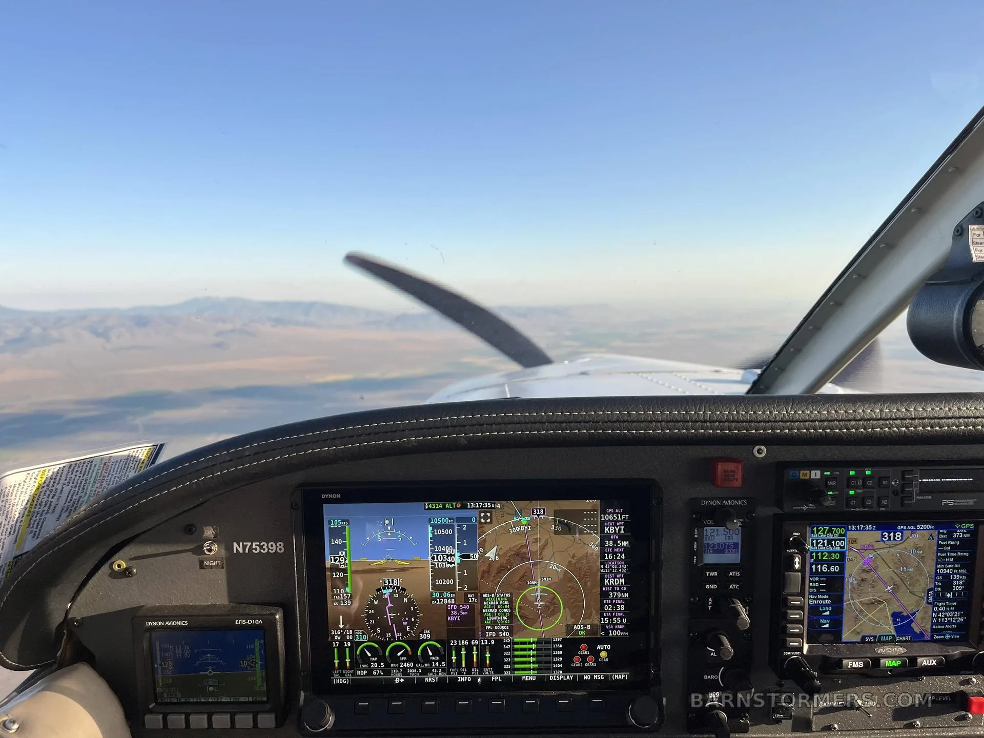 The cockpit instrument panel of a Piper Cherokee Lance (N75398) showing multiple digital displays and the view out the windshield with a propeller and distant mountains.