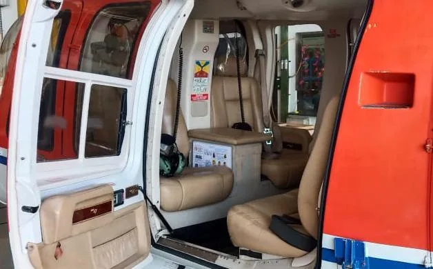 The helicopter cabin interior with tan leather seats, a center console, and an open door.