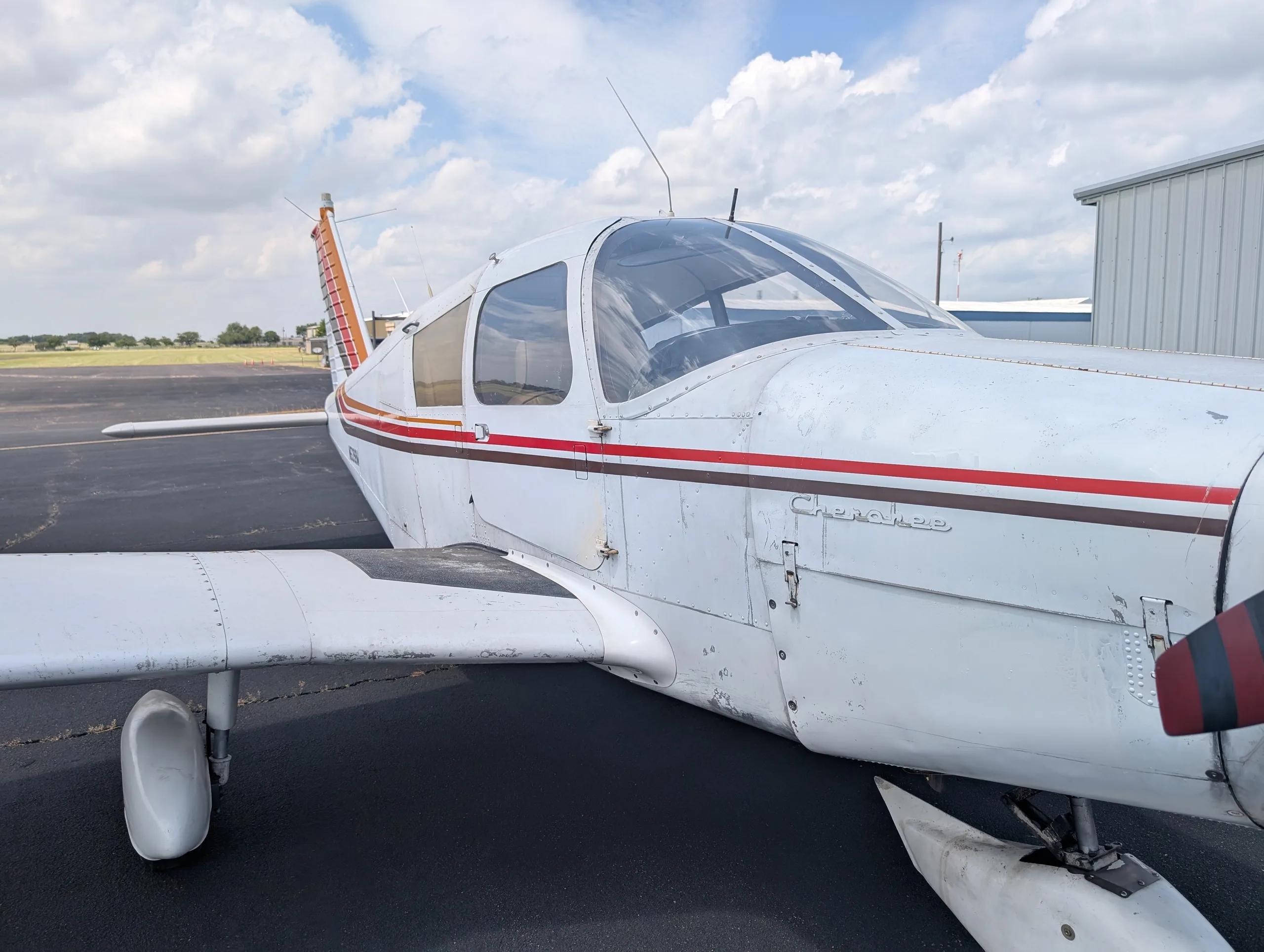A close-up view of the front fuselage of a white Piper Cherokee aircraft, showing the propeller and landing gear.