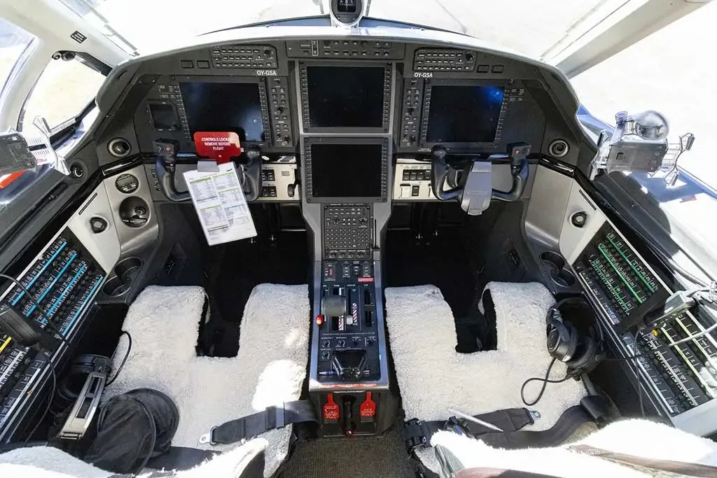 The modern cockpit of a Pilatus PC-12 aircraft, featuring multiple display screens and sheepskin seat covers.