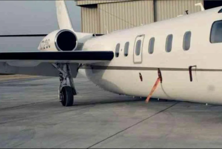 A close-up side view of a white business jet, N772DC, parked on a tarmac next to a hangar.