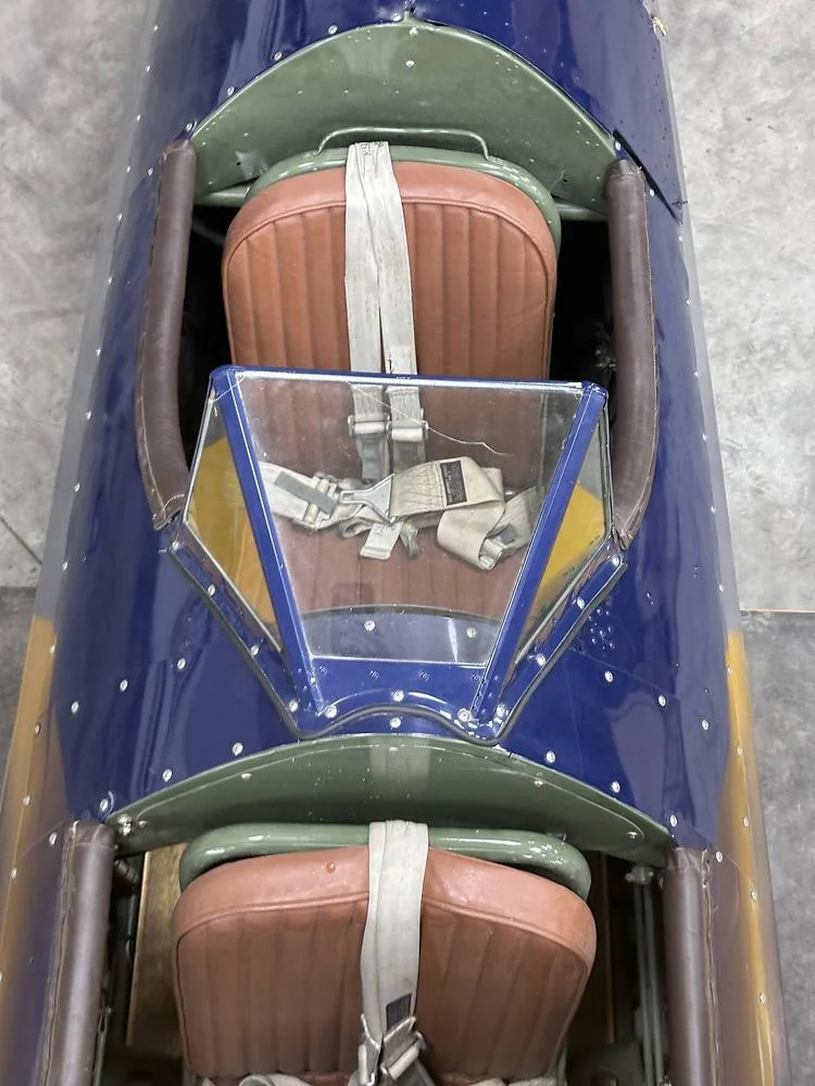 An overhead view of the two tandem cockpits of a blue biplane, showing brown leather seats and seatbelts.
