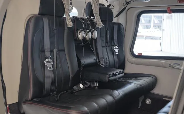 Two black leather passenger seats with headsets hanging on the headrests, inside a helicopter cabin.