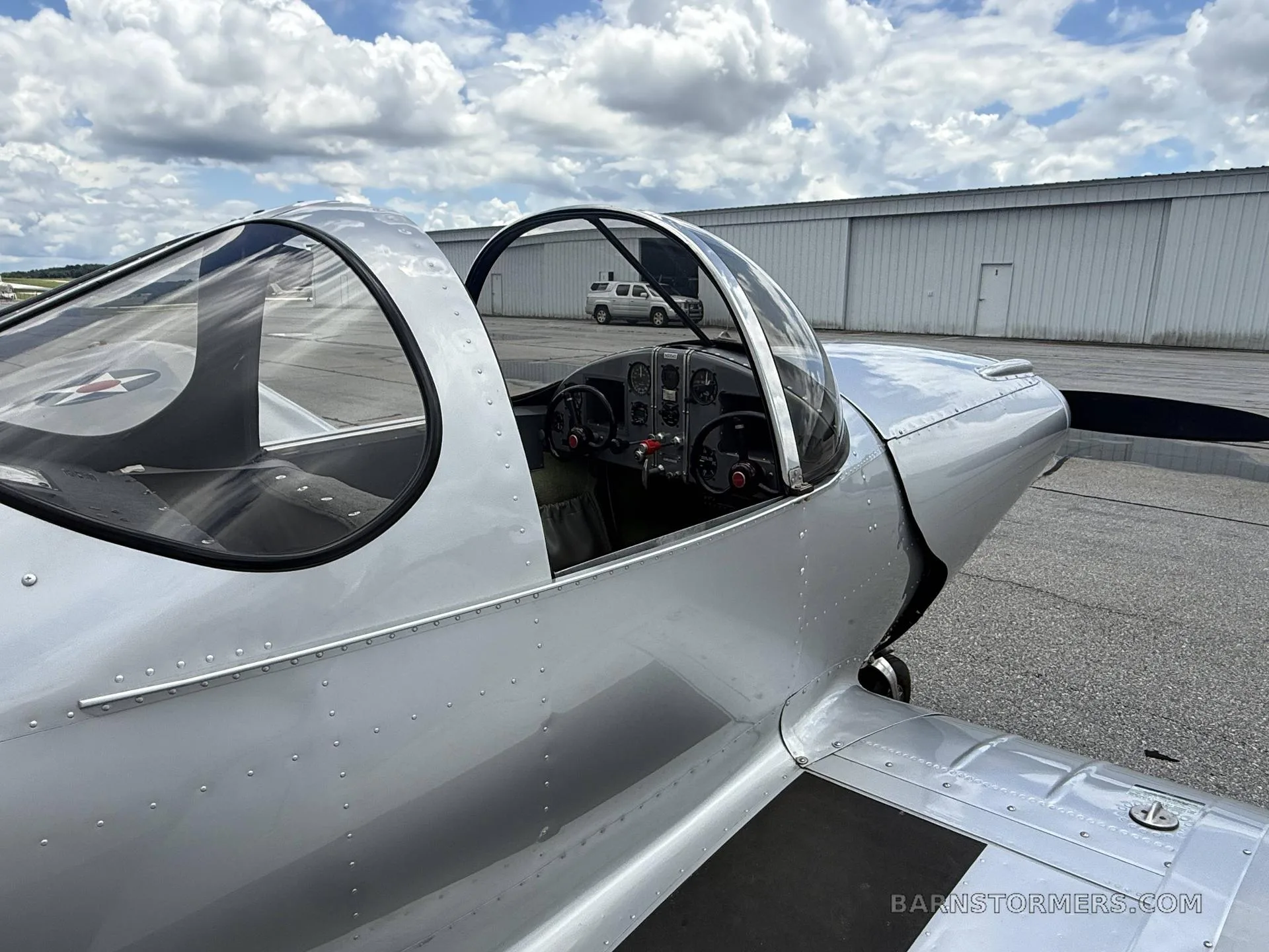 A close-up view of a silver aircraft with its bubble canopy open, revealing the cockpit and instrument panel.