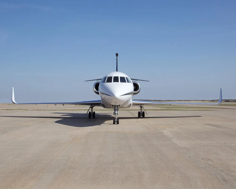 A head-on view of the white Dassault Falcon 900EX business jet with black tail and winglets parked on an airport tarmac.