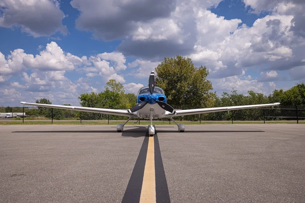 A head-on view of the blue and white Cirrus SR22 aircraft, N970S, parked on an asphalt ramp with a yellow centerline.