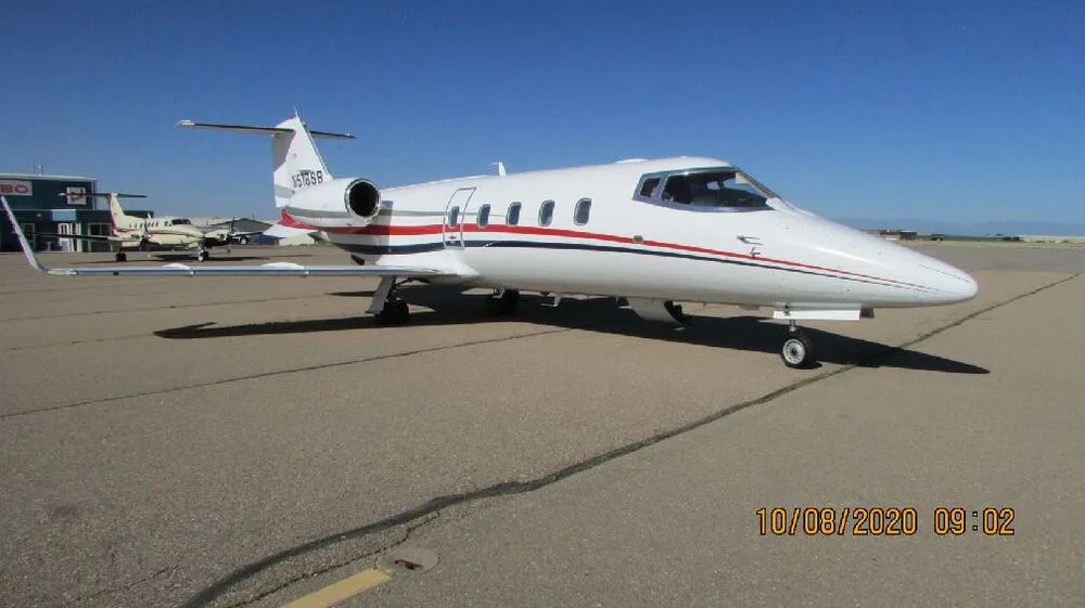 A white business jet with red and blue stripes, registration N518SB, parked on an airport tarmac under a clear sky.