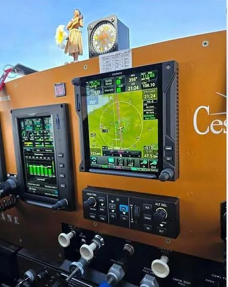 A detailed view of the modern Garmin avionics suite and control panel in the cockpit of a Cessna aircraft, with a hula dancer figurine on top.