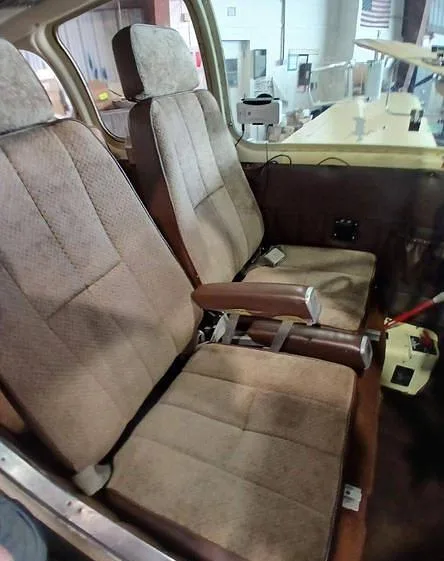 The beige fabric and brown vinyl interior seats of a small aircraft cabin.