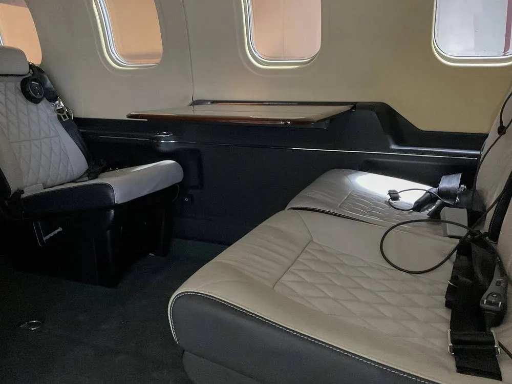 View of two light-colored, diamond-stitched passenger seats and a wooden fold-out table in an aircraft cabin.