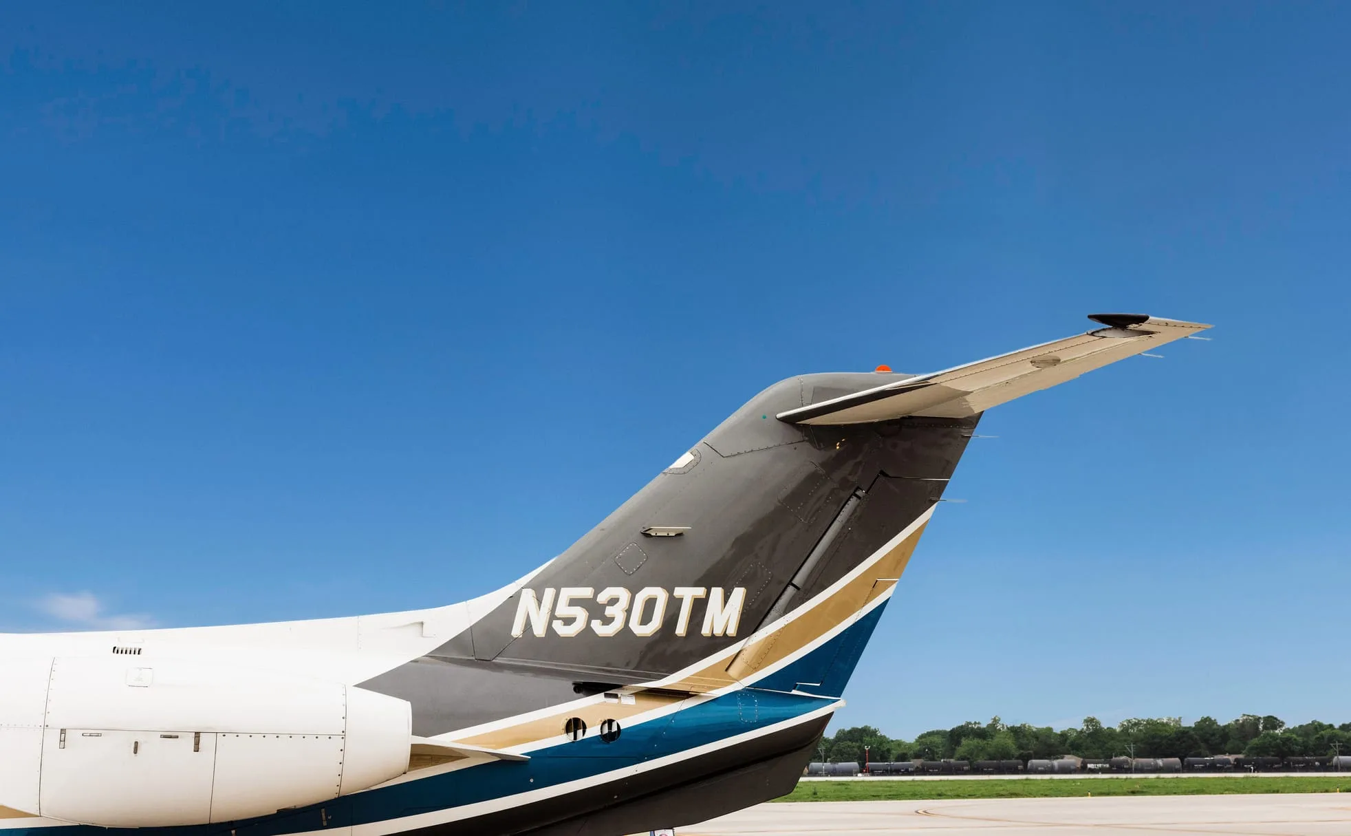 A close-up view of the tail of the N530TM private jet, showing its black, gold, and blue paint scheme against a blue sky.