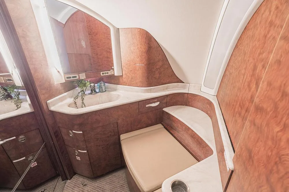The aircraft lavatory includes a sink, mirror, and toilet, all surrounded by rich wood paneling.