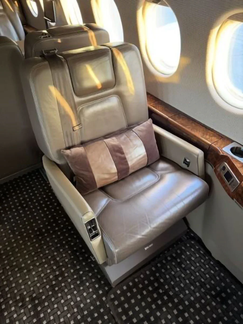 A close-up of a brown leather executive seat inside the aircraft cabin, with a striped pillow and a window.