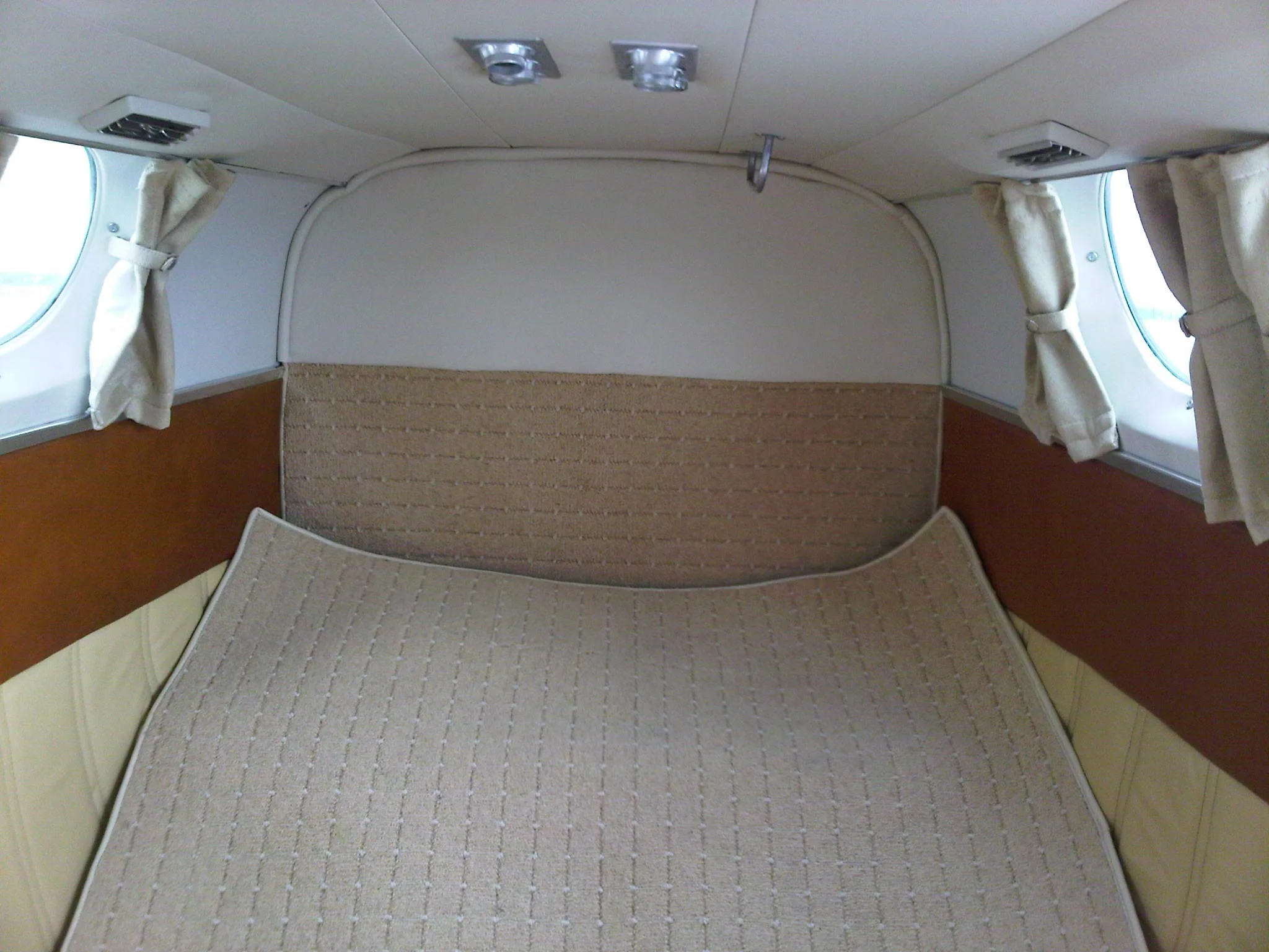 The rear cabin of an aircraft configured with a beige upholstered bed, surrounded by light-colored walls and windows with curtains.