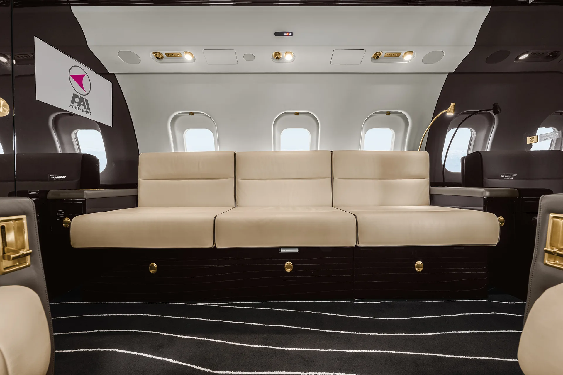 A close-up view of a three-seat cream leather sofa in a private jet cabin, with dark wood paneling and a striped carpet.